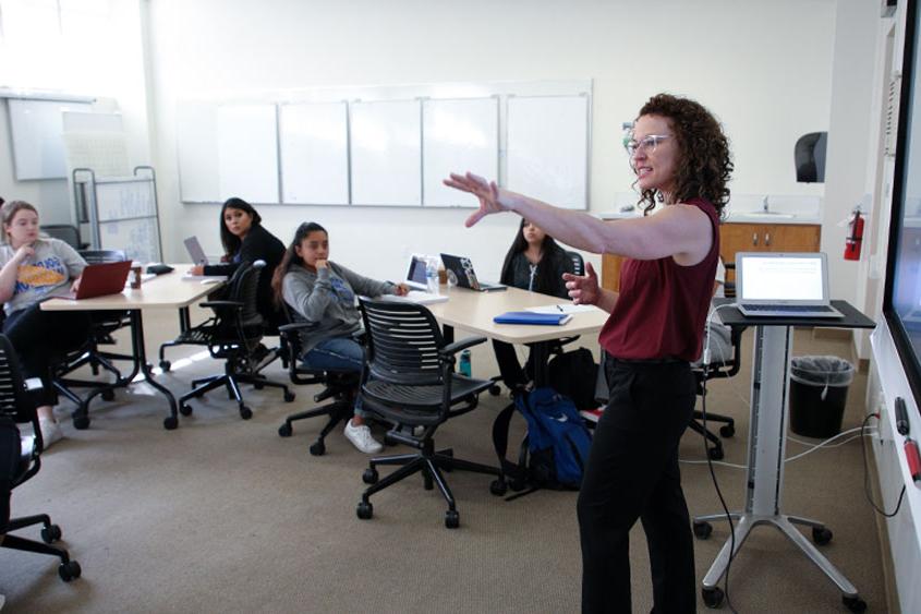 A professor holds out her arm towards the classroom as she speaks.